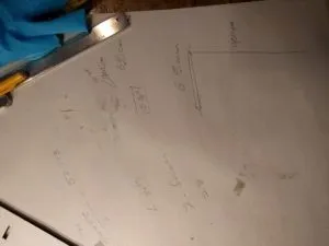 White paper fills the page. In black pen, there are lines an measurements scrawled over the page. In the upper left sits the bottom half of a pencil and a set of mechanical calipers.