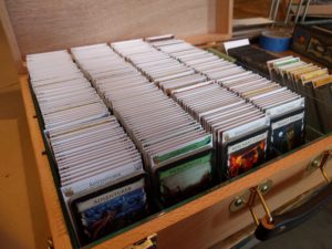 Open wooden box displaying contents consisting of rows of Dominion cards separated by labeled dividers. 