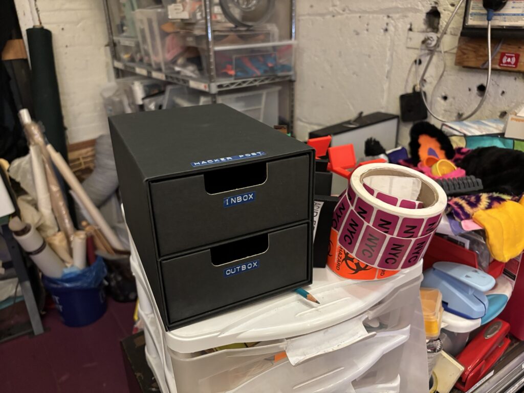 A small gray cardboard mini chest with two drawers, labeled "inbox" and "outbox." The box itself is labeled "Hacker Post."